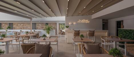 A modern outdoor dining area with multiple tables and chairs, a bar area, and a view of the surrounding landscape.