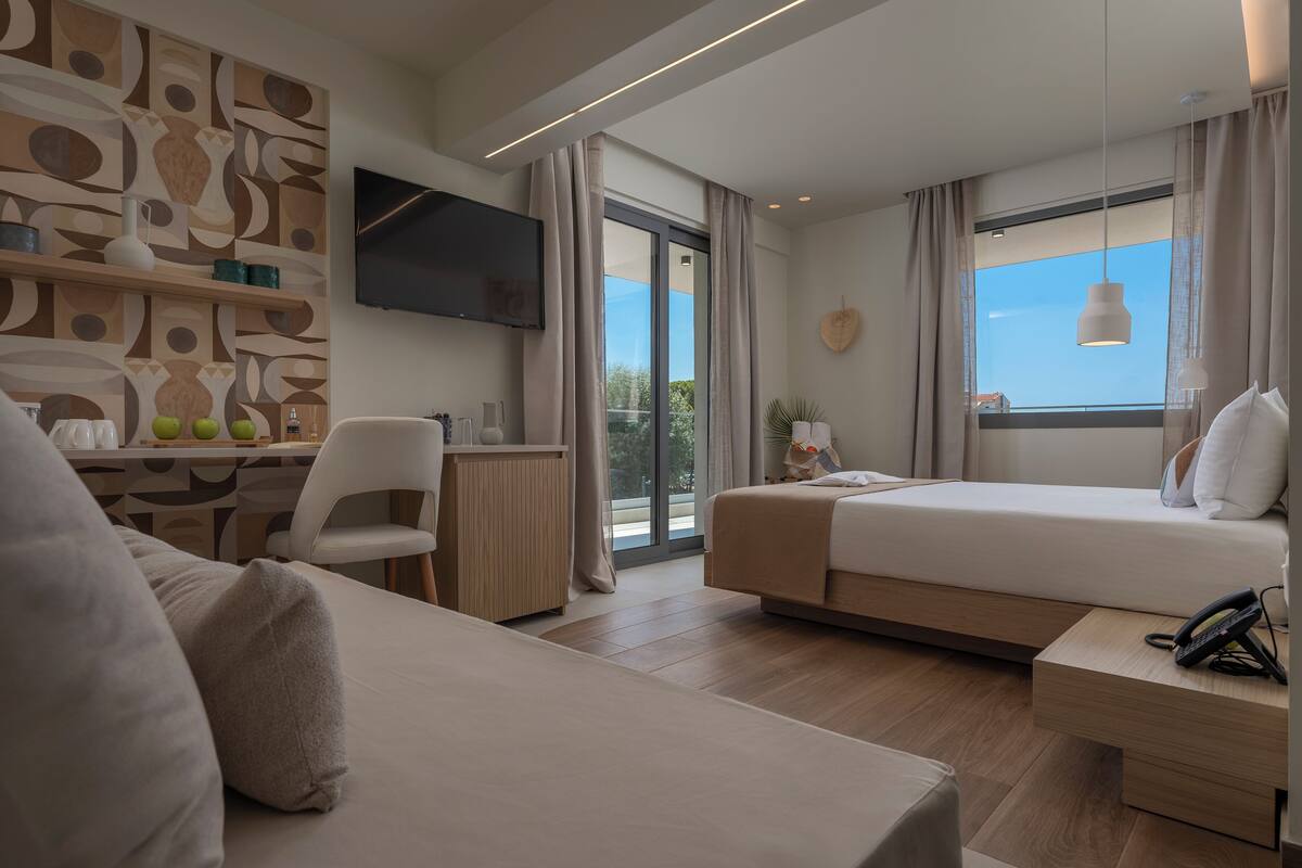 A modern hotel room with a large bed, a desk with a chair, a TV, and a view of the outdoors.