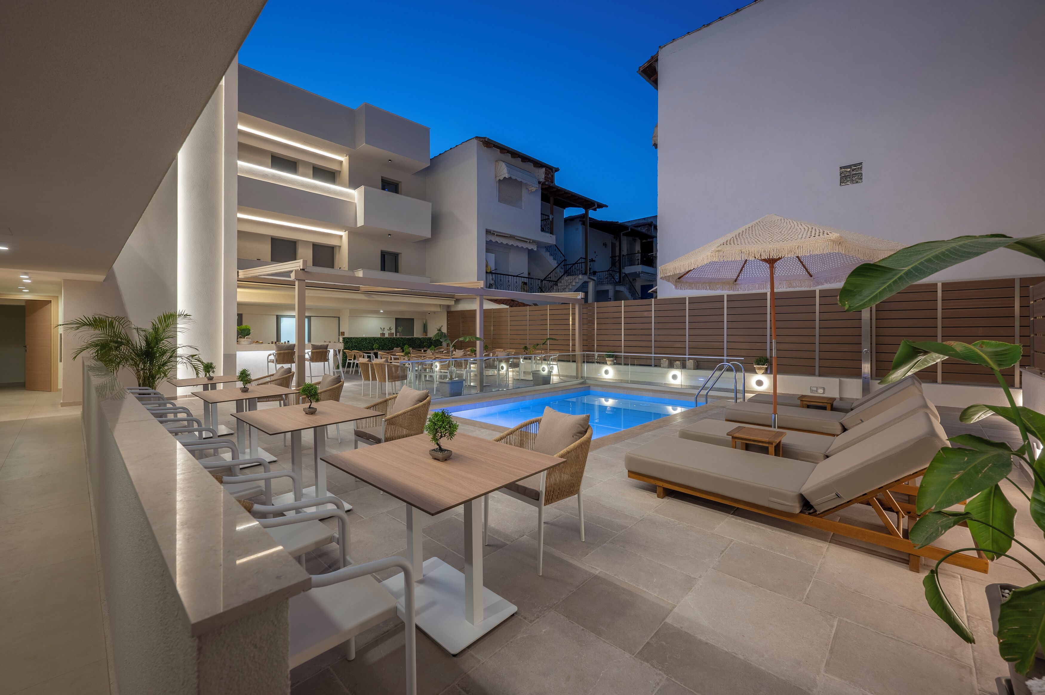 A modern outdoor pool area with lounge chairs and tables, surrounded by buildings.