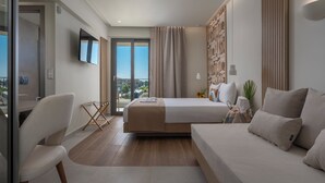 A modern hotel room with a bed, a sofa, a TV, and a balcony with a city view. - Sandy Seaside Suites (Nea Propontida)