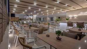 A modern cafe with wooden tables and wicker chairs, featuring a ceiling with recessed lighting and a wall with a motivational quote. - Sandy Seaside Suites (Nea Propontida)