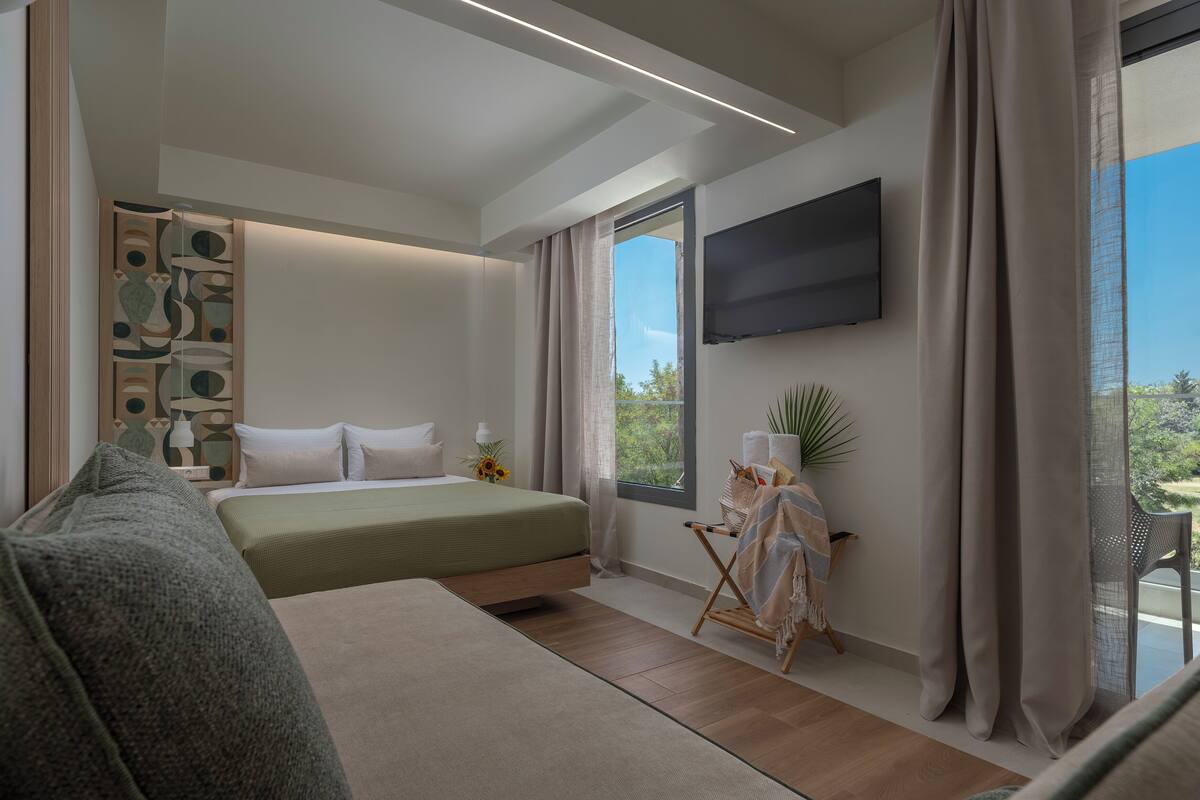 A modern bedroom with a bed, a seating area, a flat-screen TV, and a balcony with curtains.