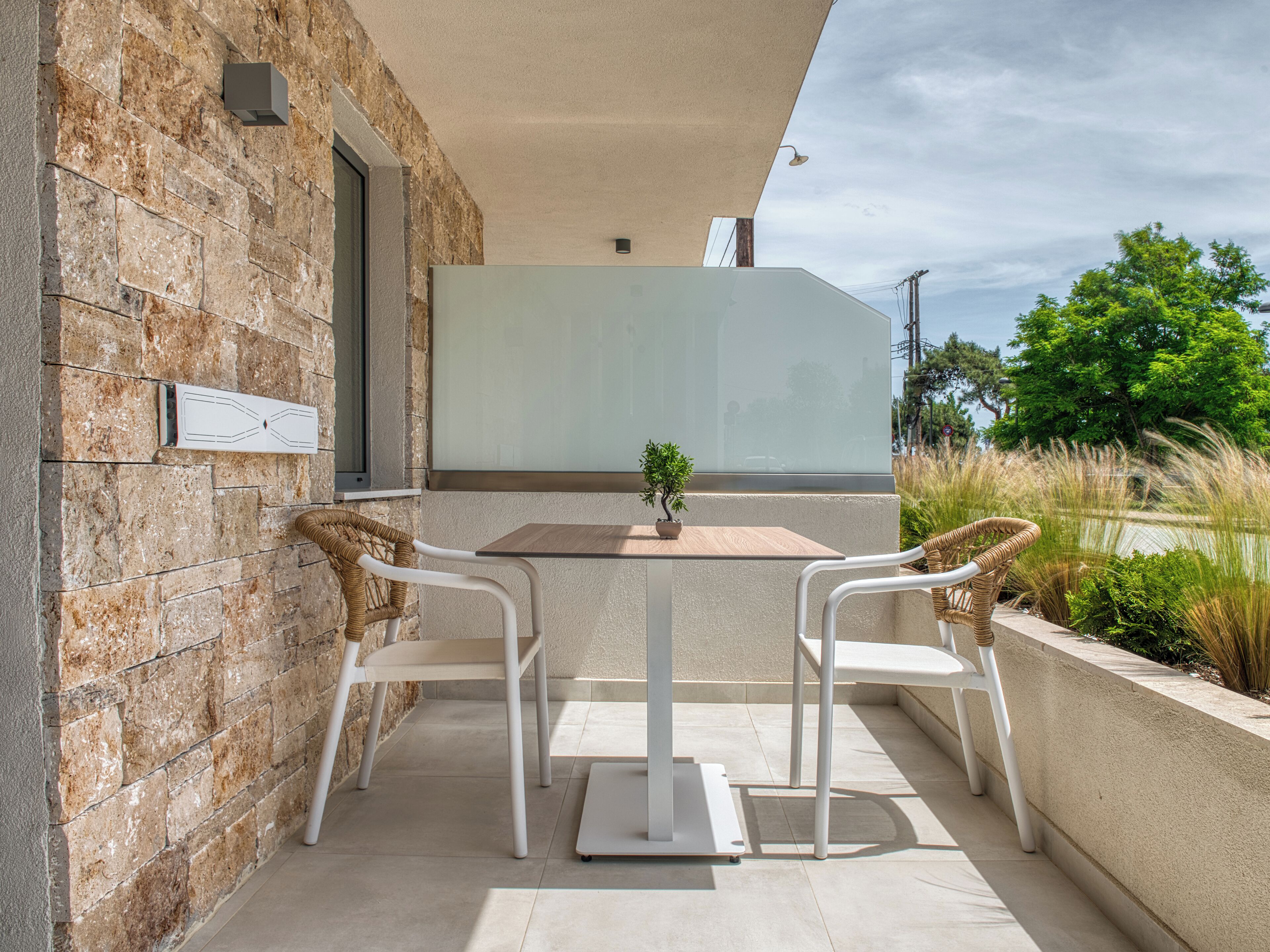 A patio with two white chairs and a table, a potted plant, and a stone wall.