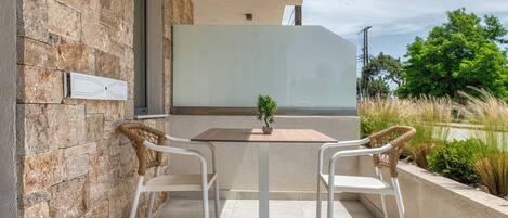 A patio with two white chairs and a table, a potted plant, and a stone wall.