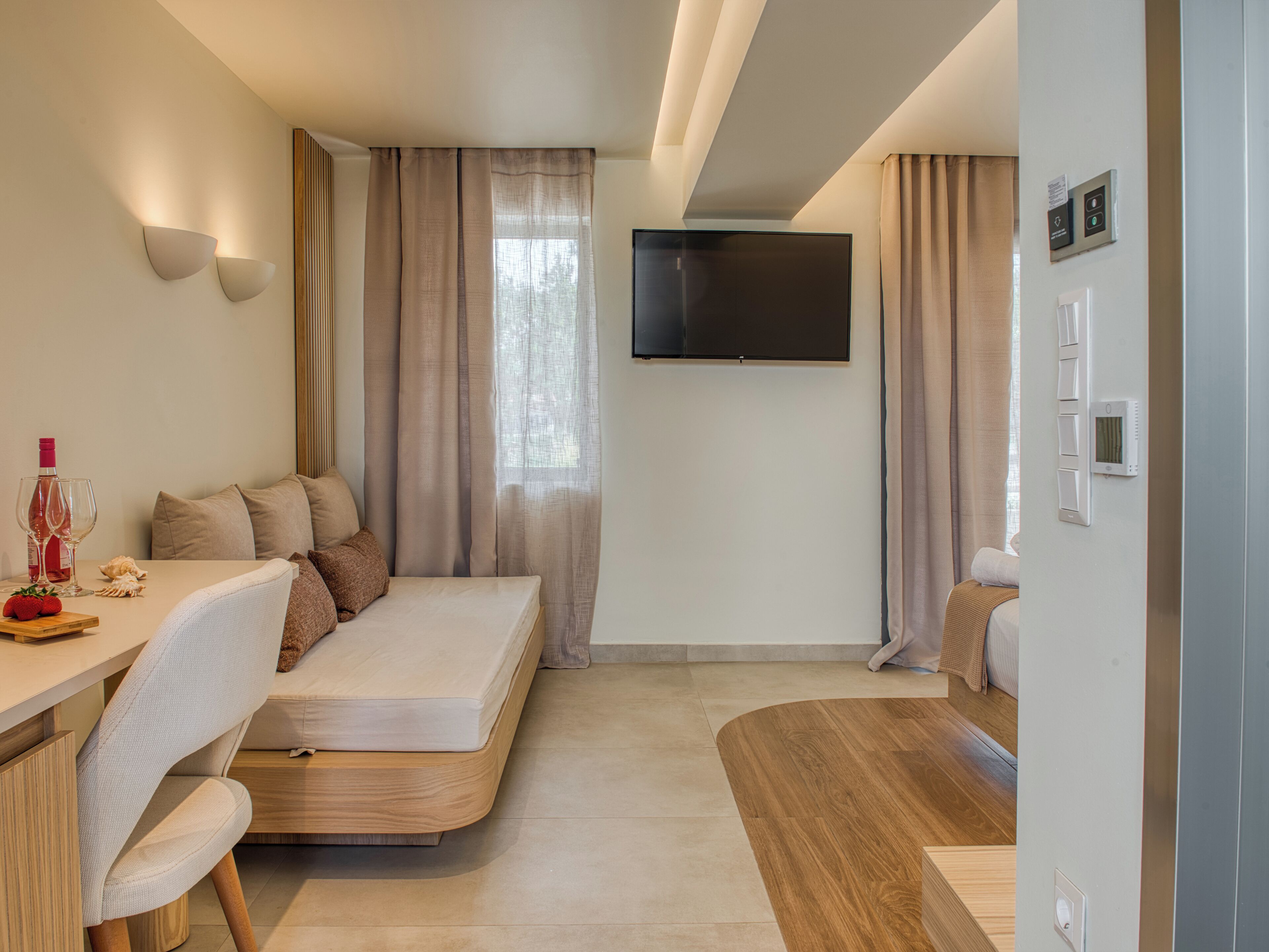 A modern hotel room with a bed, a desk, a TV, and a control panel.