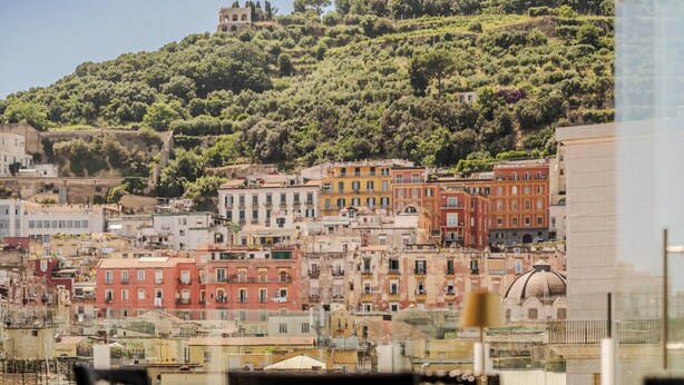 A coastal cityscape with historic buildings, a hilltop fortress, and a view of the sea. - Hotiday Room Collection - Napoli Diaz (Naples)