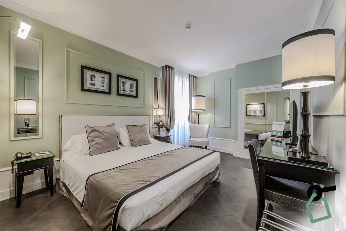 A hotel room with a large bed, bedside tables, a desk, and a chair.