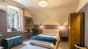 Un dormitorio con cama, candelabro, ventana con cortinas, mesita de noche y puerta de madera.