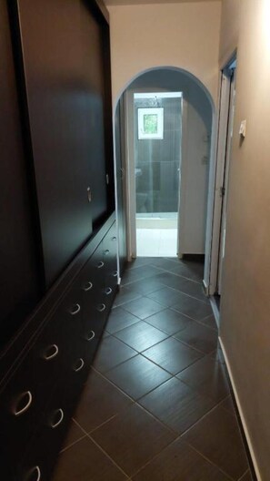 A hallway with a tiled floor and a door leading to a room with a shower. - Lovely Urban Retreat (București)