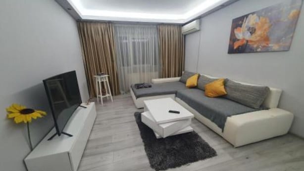A modern living room with a sofa, a coffee table, a TV, and a painting on the wall. - Lovely Urban Retreat (București)