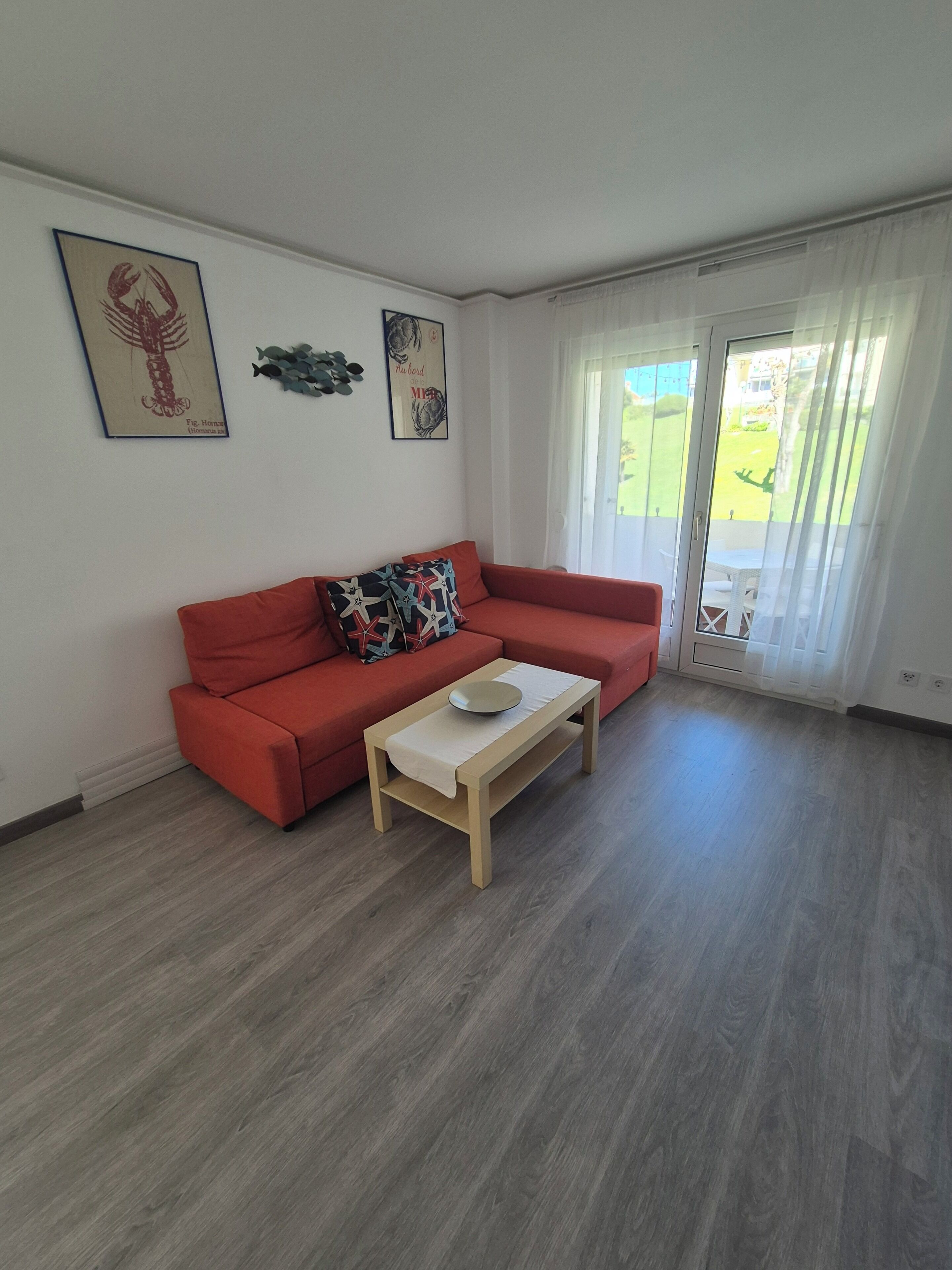 Ein Wohnzimmer mit einem roten Sofa, einem Holztisch und einer Glastür, die zu einem Außenbereich führt.