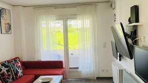 Een woonkamer met een rode bank, een salontafel, een televisie en een schuifdeur naar een balkon.