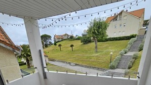 Een balkon met een witte tafel en stoelen, uitzicht op een woonwijk en lichtjes.