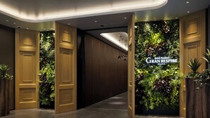 A hotel lobby with wooden doors, a green wall with plants, and a sign reading "Hotel Hankyu Gran Respire".