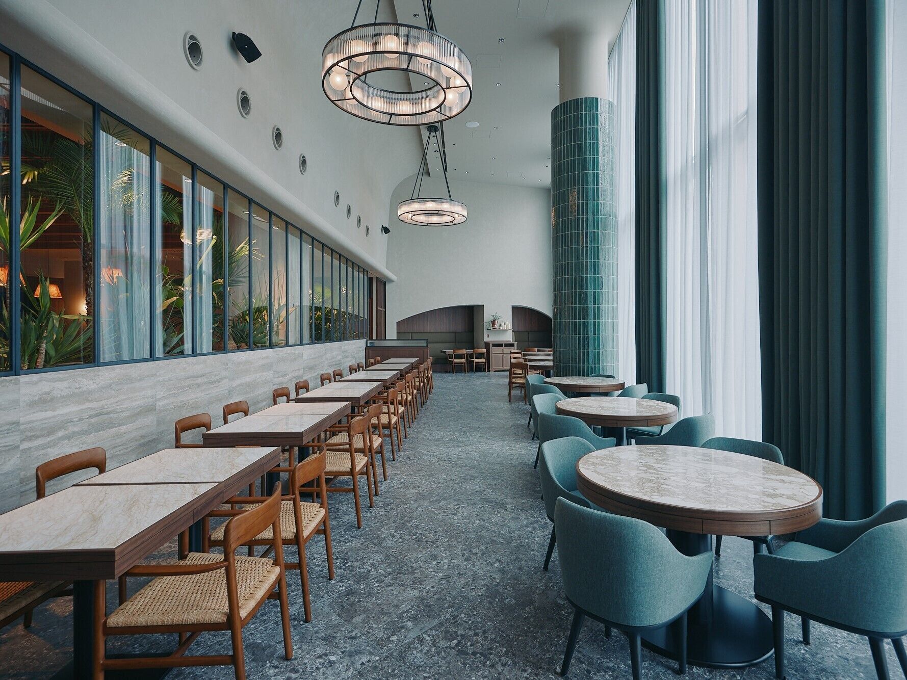 A modern hotel lobby with long tables and chairs, a large pillar, and a view of the outdoors.