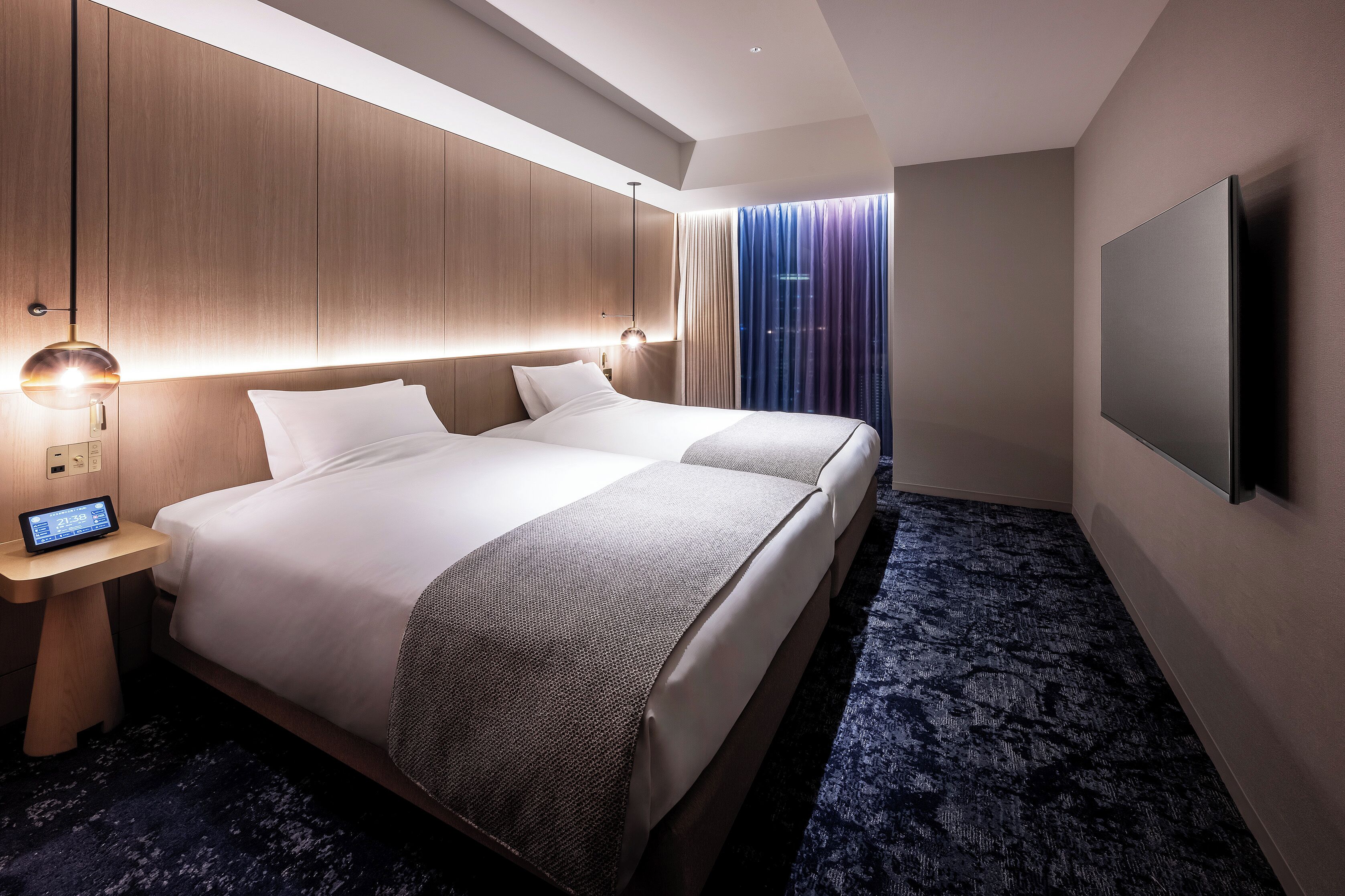 A modern hotel room with a large bed, bedside tables, a flat-screen TV, and a city view.