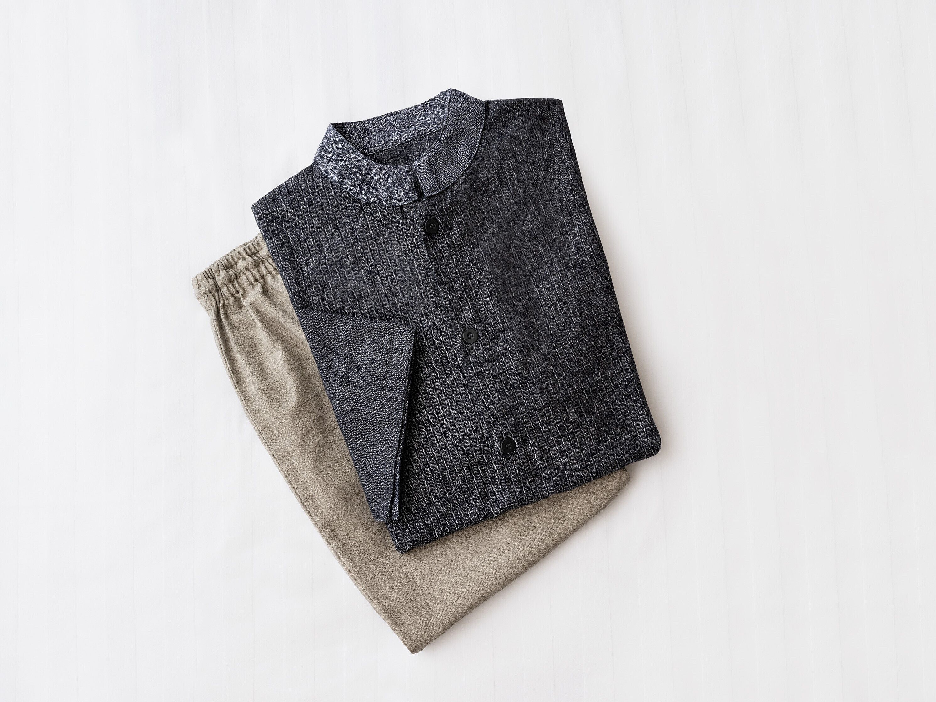 A neatly folded dark-colored shirt with a collar and buttons, placed on a light-colored fabric.