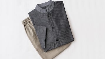 A neatly folded dark-colored shirt with a collar and buttons, placed on a light-colored fabric.