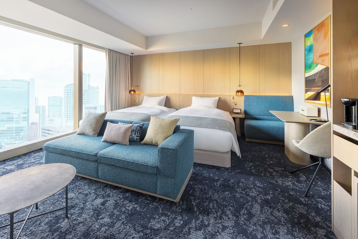 Quarto de hotel com uma cama grande, um sofá, uma escrivaninha e vista para a cidade.