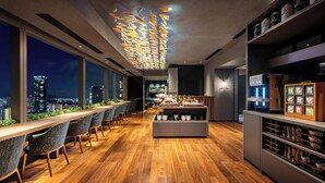 A modern bar area with a wooden floor, bar stools, a water dispenser, and a view of the city at night.