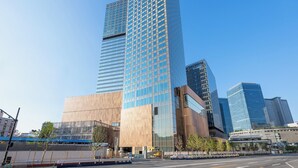 A modern high-rise building with a glass facade, surrounded by other tall buildings and a clear blue sky.