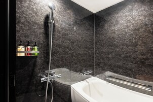 A modern bathroom with a glass-enclosed shower, a white bathtub, and a marble wall.