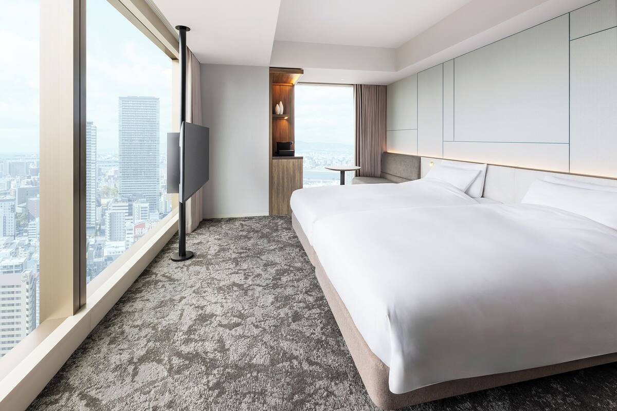 Quarto de hotel moderno com uma cama grande, televisão e vista para a cidade.