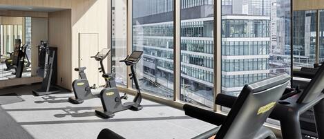 A modern gym with exercise equipment and large windows offering city views.