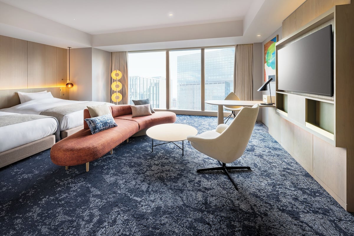 Quarto de hotel moderno com uma cama grande, um sofá, uma mesa redonda e uma TV fixada na parede.