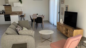 A modern living room with a sofa, a pink chair, a TV, and a dining area with a table and chairs. - Modern family home, close to beaches and garrigue (La Palme)