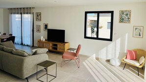 A living room with a sofa, a chair, a TV on a wooden stand, and artwork on the walls. - Modern family home, close to beaches and garrigue (La Palme)