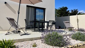 An outdoor patio with a table and chairs, a large umbrella, and a garden with lavender plants. - Modern family home, close to beaches and garrigue (La Palme)