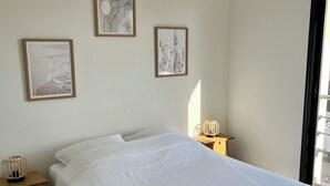 A bedroom with a large bed, a bedside table with a lamp, and framed pictures on the wall. - Modern family home, close to beaches and garrigue (La Palme)