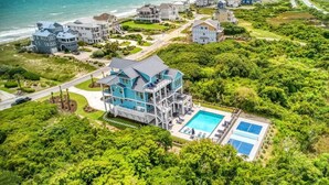 En fastighet vid kusten med ett stort hus, en pool och utsikt över havet.