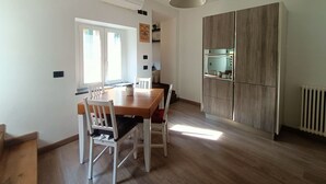 A dining area with a wooden table and white chairs, a pendant light, and a built-in kitchen cabinet with a microwave. - Delle Erbe The Nightlife (Albenga)