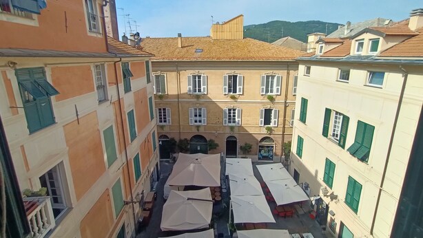 A courtyard with multiple buildings, outdoor seating, and a view of a mountain. - Delle Erbe The Nightlife (Albenga)
