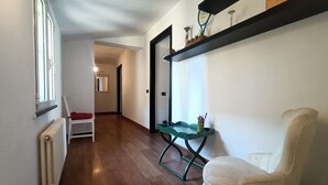 A hallway with a radiator, a white chair, a green table, and a shelf with decorative items. - Delle Erbe The Nightlife (Albenga)