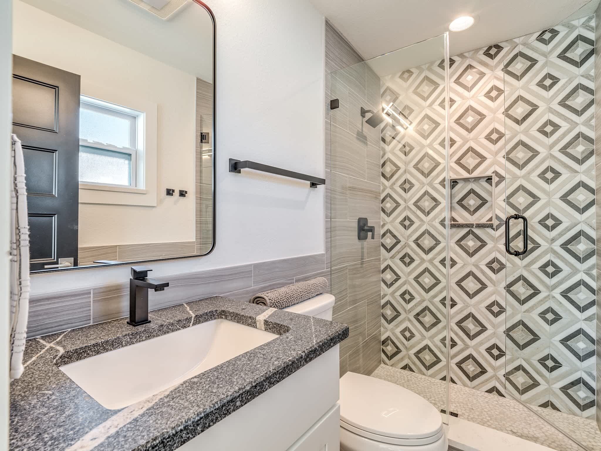 Un bagno con lavabo in granito, servizi igienici e doccia con piastrelle decorate.