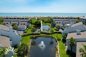 Een resort met meerdere gebouwen, een vijver in het midden en uitzicht op het strand.