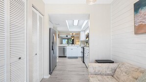 A hallway leading to a kitchen with white cabinets, a refrigerator, and a ceiling fan. - Exclusive End-Unit! Sea Winds #36: Gated Ocean Views & Direct Beach Access! (St. Augustine Beach)
