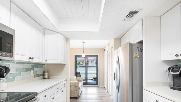 A kitchen with white cabinets, a stainless steel refrigerator, and a microwave. - Exclusive End-Unit! Sea Winds #36: Gated Ocean Views & Direct Beach Access! (St. Augustine Beach)