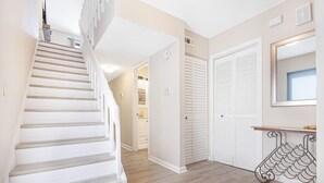 A staircase leading to a second floor, a hallway with a mirror, and a door with louvered shutters. - Exclusive End-Unit! Sea Winds #36: Gated Ocean Views & Direct Beach Access! (St. Augustine Beach)