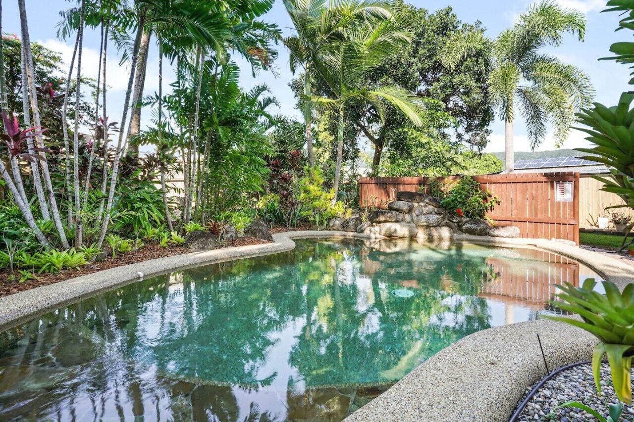 Una piscina rodeada de follaje tropical y una cerca de madera.