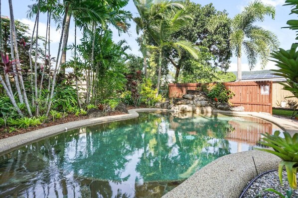 Una piscina rodeada de follaje tropical y una cerca de madera.