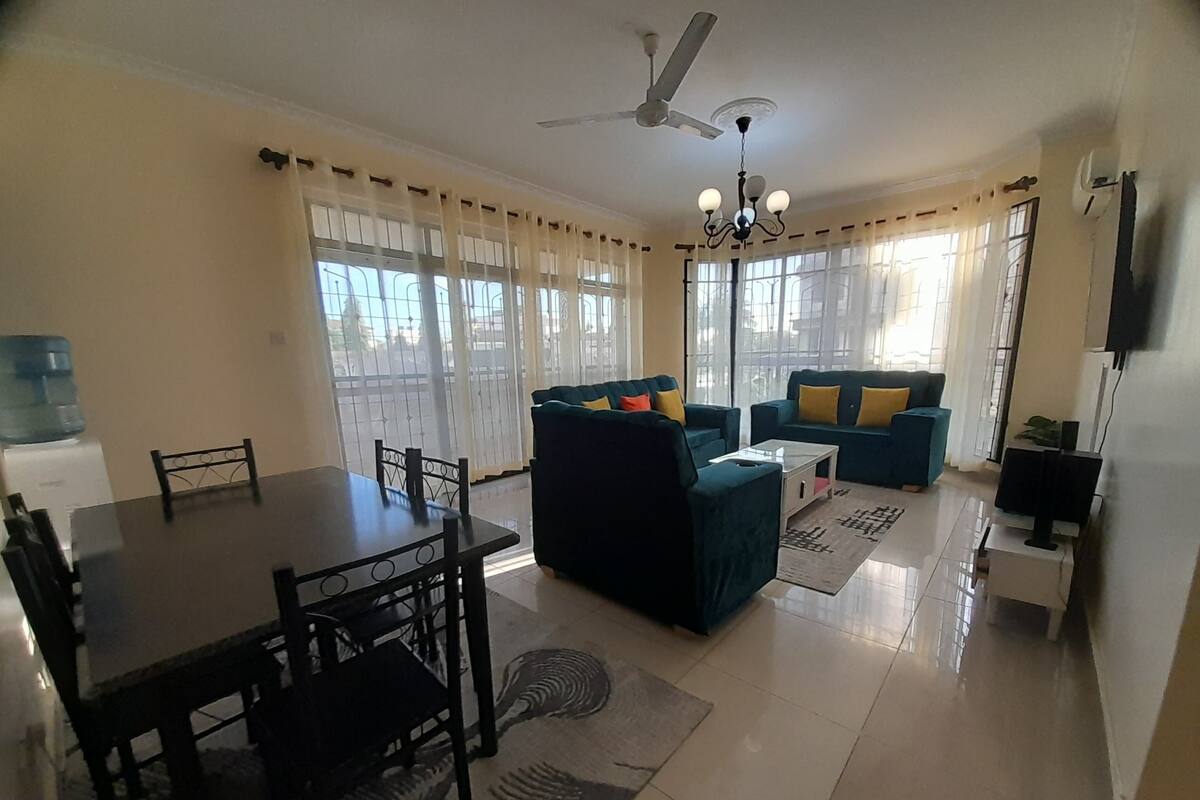 Uma sala de estar com uma mesa de jantar, dois sofás, um ventilador de teto e uma televisão.
