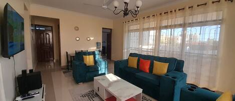 Una sala de estar con un conjunto de sofá, una mesa de centro, un televisor y un comedor al fondo.