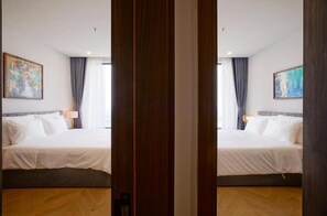 Habitación de hotel con dos camas, un ventanal con cortinas y cuadros en las paredes.