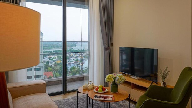 Une chambre d’hôtel moderne dotée d’une grande fenêtre, d’un téléviseur à écran plat, d’un fauteuil vert, d’une petite table ornée d’un vase de fleurs et d’un canapé.