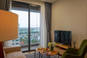 Ein modernes Hotelzimmer mit großem Fenster, einem Flachbildfernseher, einem grünen Sessel, einem kleinen Tisch mit Blumenvase und einer Couch.