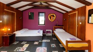 Una habitación con dos camas, vigas de madera, una pared morada y un espejo con forma de corazón, además de una ventana.